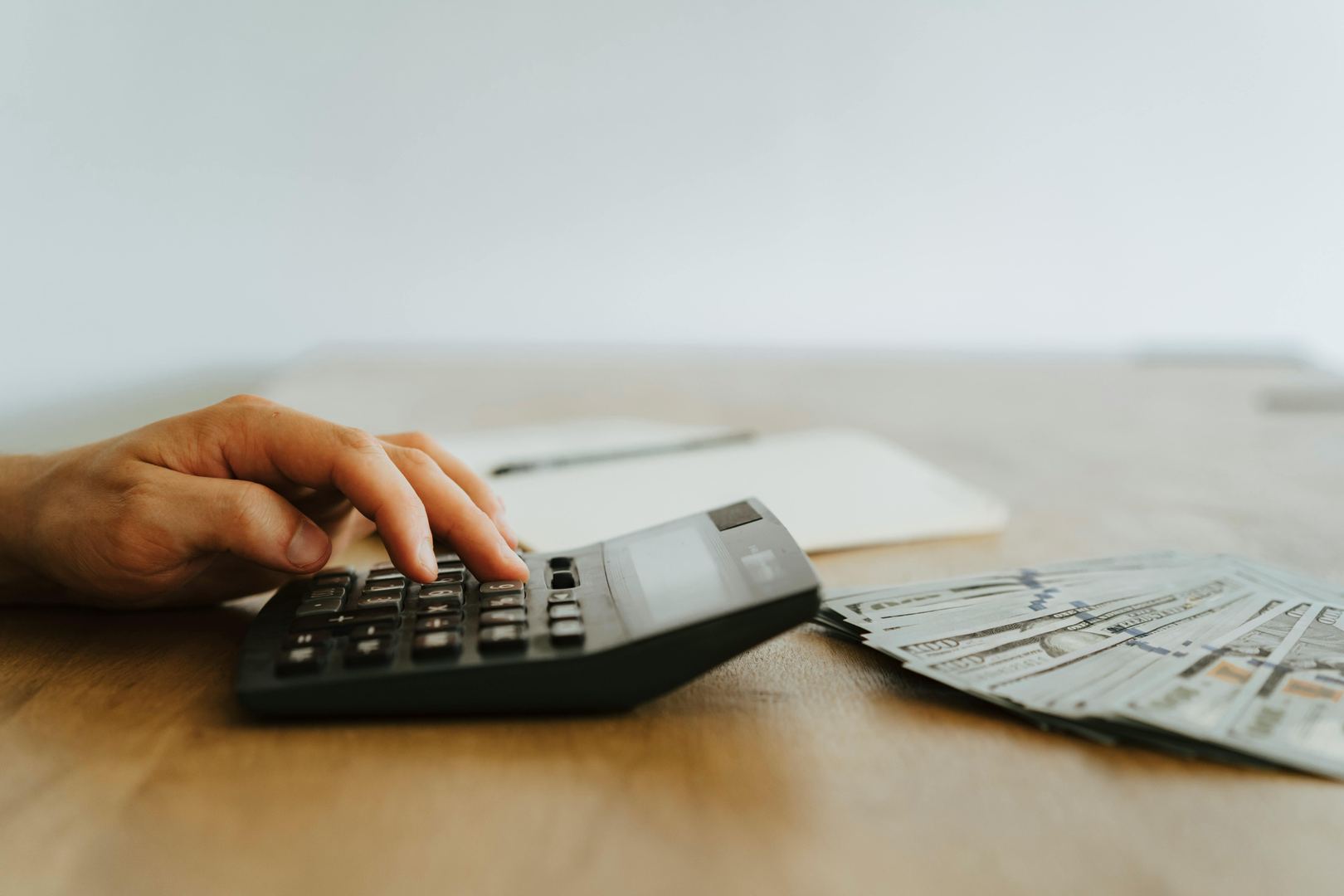 Hand on calculator with cash, representing the 15% administrative budget constraint